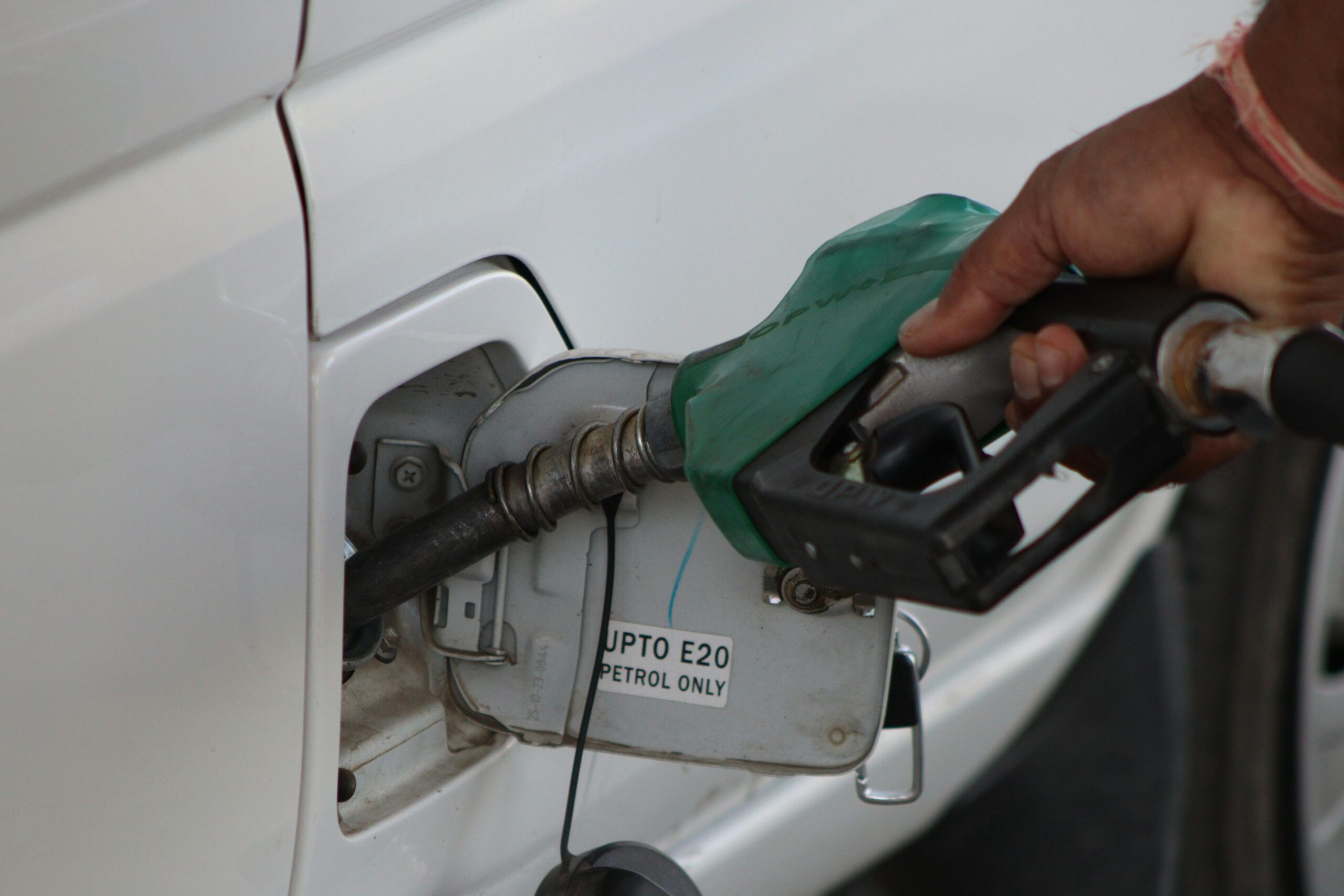 Hand refueling car with E20 petrol at a gas station, close-up view.