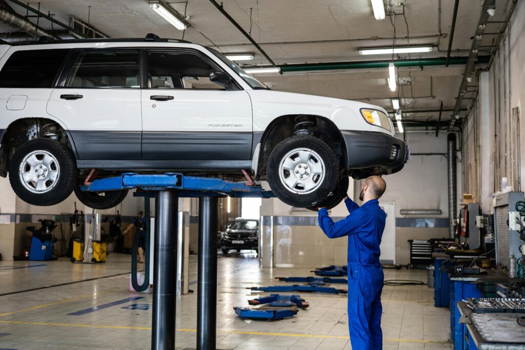pexels photo 8986070 8986070 A mechanic inspecting a white SUV lifted in a well-lit auto repair shop.